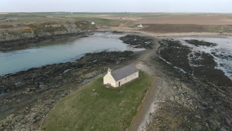 An-aerial-view-of-Eglwys-Cwyfan-church-on-an-overcast-day,-flying-left-to-right-around-the-church,-Anglesey,-North-Wales,-UK