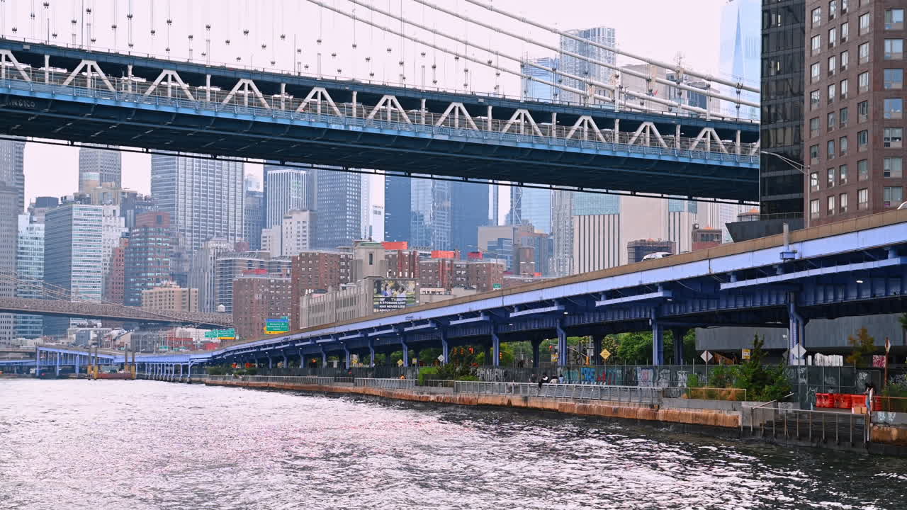 Auto in movimento sull'autostrada lungo il lungomare dell'East River. Vista dal basso verso l'alto del Manhattan Bridge a New York, USA, dal fiume