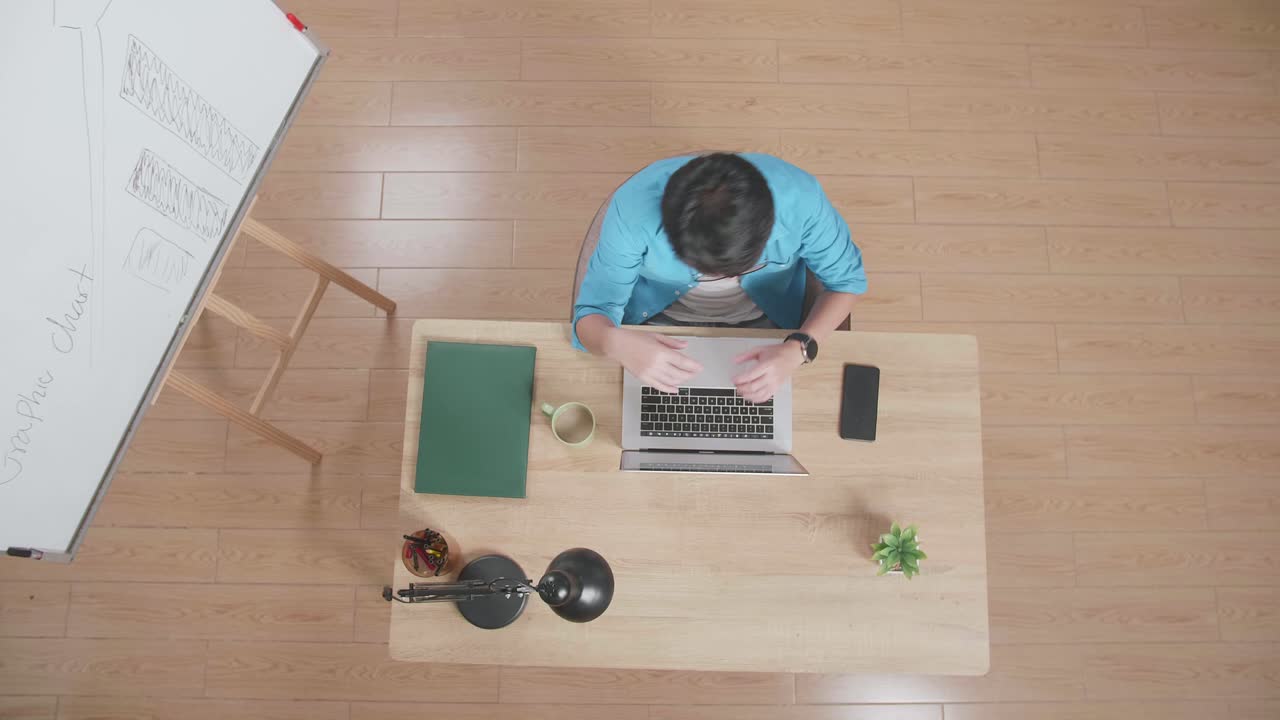 뷰  아웃은 머리가 아파서 지친 남자가 집에 있는 화이트보드 의 나무 책상에 앉아 스마트폰 의 노트북에서 타이핑하는 장면입니다.