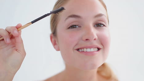 una mujer rubia sonriente cepillándose las cejas.