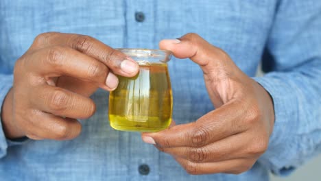 close up of a man's hands holding a small glass bottle of yellow oil