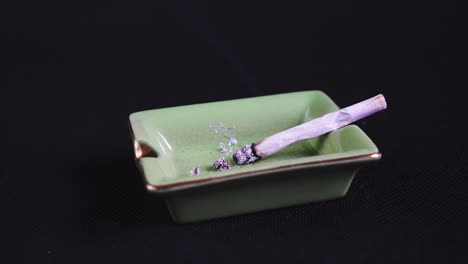 smoking and ashing a rolled cigarette or joint, legalised marijuana on green ashtray