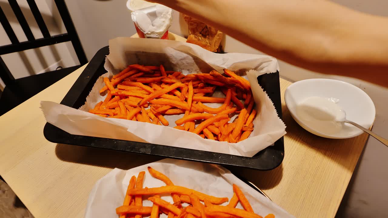 En hånd drysser salt over varme pommes frites i et simpelt køkken i en lejlighed fra Sovjet-tiden