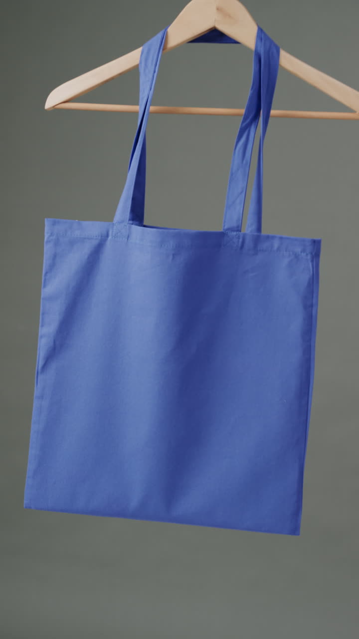 Vertical video of hanger with blue canvas bag and copy space on grey background