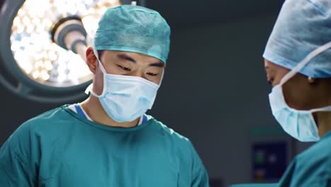 two surgeons, dressed in scrubs and masks, discuss the details of an intricate surgical procedure in a state-of-the-art operating room during a busy day.