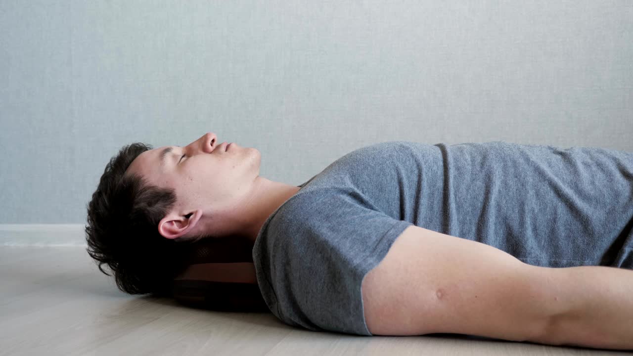 피곤한 남자가 전기 마사지 베개로 바닥에 누워있다