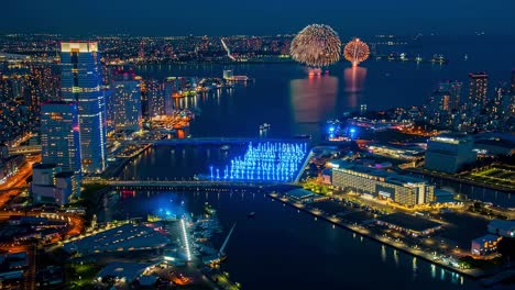 vibrant fireworks bursting over illuminated modern cityscape, reflecting luminous architecture and bridges across nighttime water surface