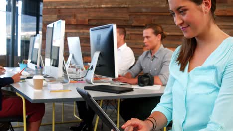 Female-business-executive-using-digital-tablet-while-colleague-working-at-desk