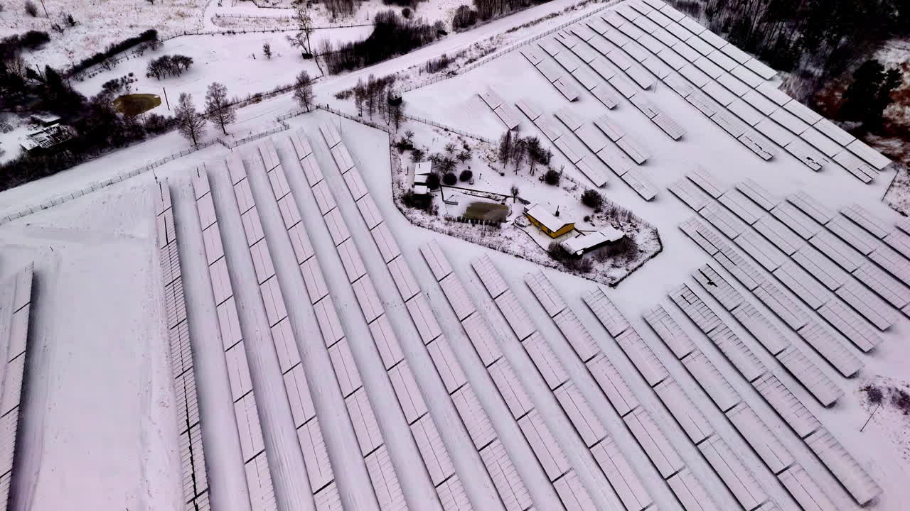Aerial view of a country house surrounded by a solar farm under a blanket of snow.