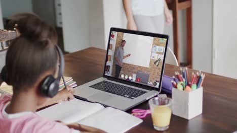 Diverse-schoolgirl-having-class-on-laptop-video-call-with-male-teacher-in-slow-motion