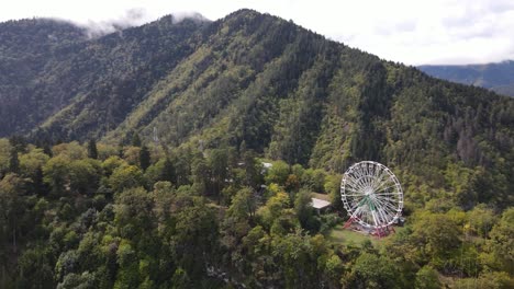 vista aérea de la rueda gigante en la cima de las montañas rodeada de bosque nube niebla valle ciudad
