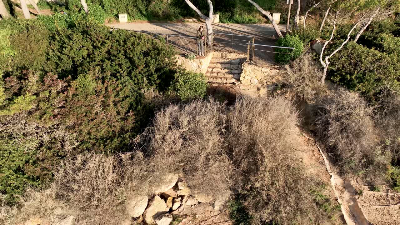 adolescente descansando en un mirador rodeado de vegetación, mirando el mar turquesa mojando las rocas del acantilado