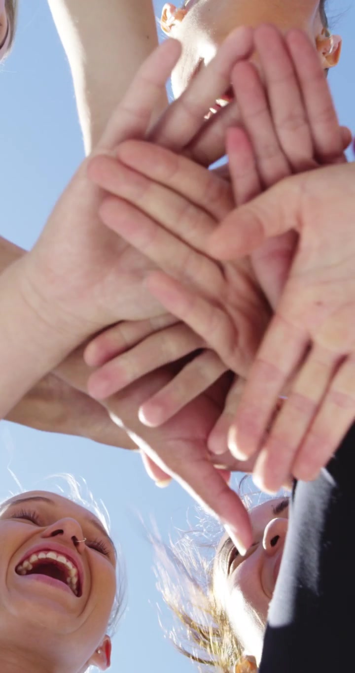 Grupo de amigos felices apilando las manos juntos contra un cielo azul despejado