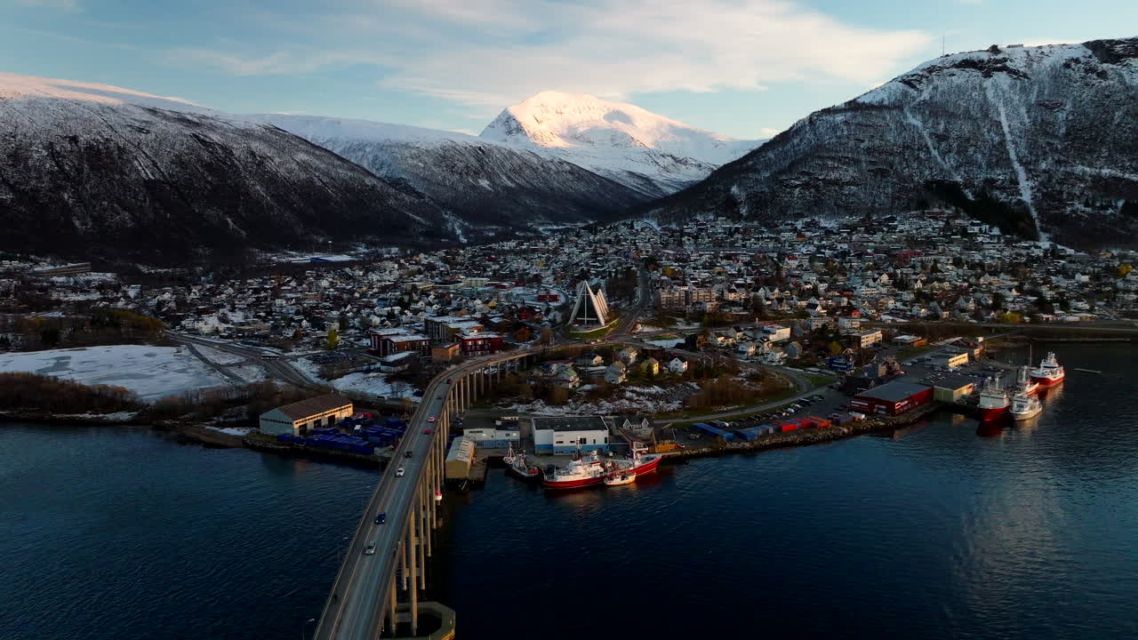 Panoramatický letecký pohled na centrum města Tromsø a most spojující s Arktickou katedrálou. Zimní krajina na začátku zimy s lehkým sněhem na horách. Ideální pro skandinávskou turistiku a architekturu
