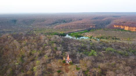 Toma-Aérea-De-Un-Templo-Hindú-Con-Un-Río-Cubierto-De-Densos-Bosques-Semiáridos-Y-Colinas-A-Su-Alrededor-En-La-Zona-De-Shivpuri-De-Madhya-Pradesh,-India