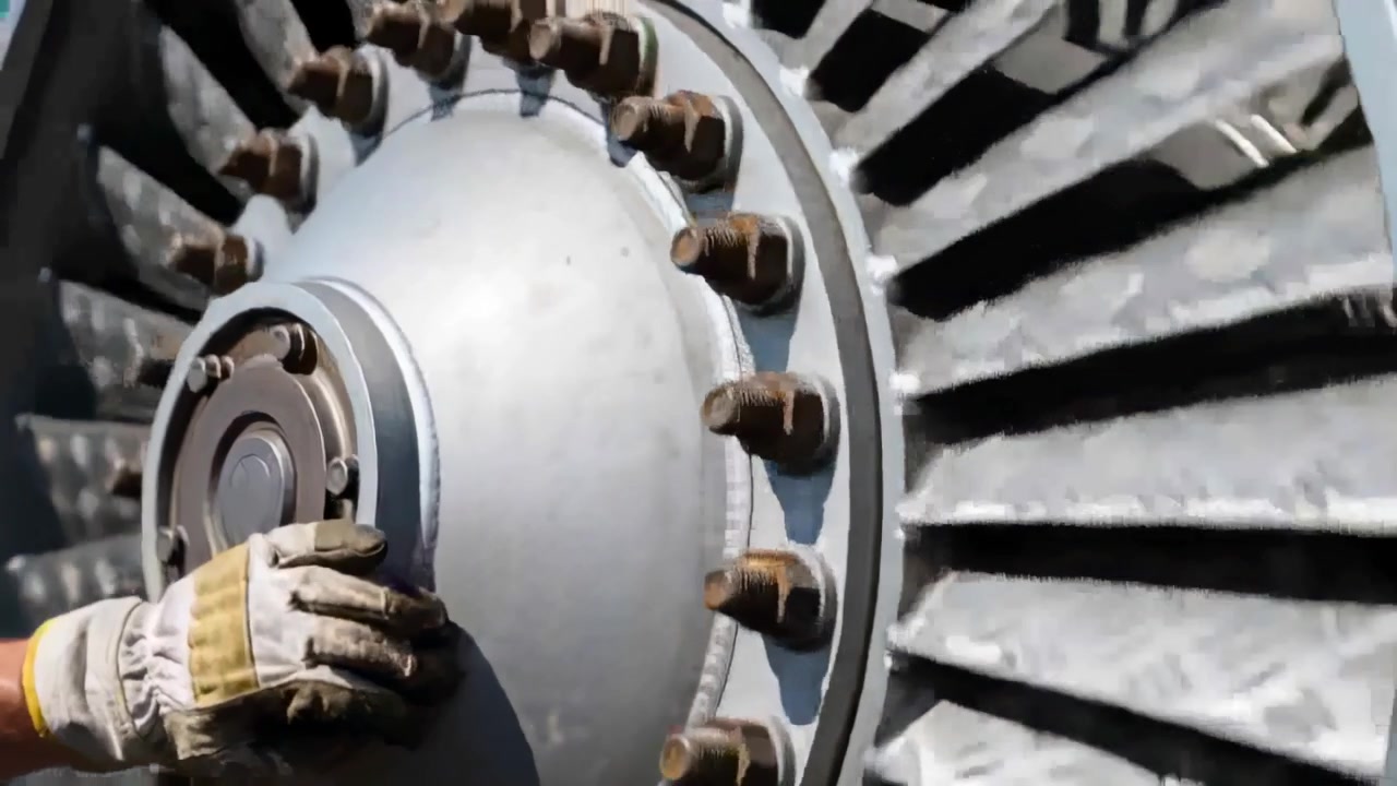 Technik v rukavicích se dotýká centrálního krytu a otáčí jím u náboje střešní turbíny, přistupuje k ložisku pro kontrolu.