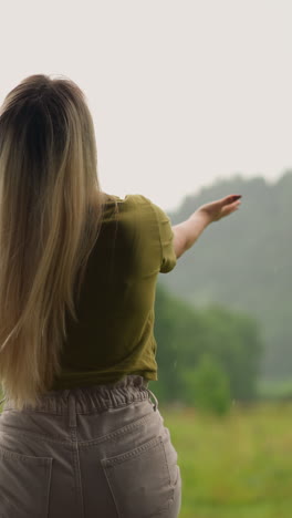 feliz mujer rubia disfruta de la unidad con la naturaleza bajo la lluvia de verano sentada en la valla en el complejo ecológico de highland en un día nublado vista trasera en cámara lenta