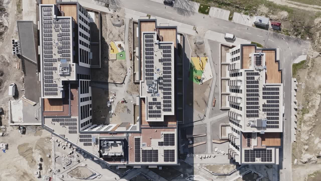 Construction site of new apartments with photovoltaic solar panels on the roof. Aerial top down view. Ecological houses of the future. 4K