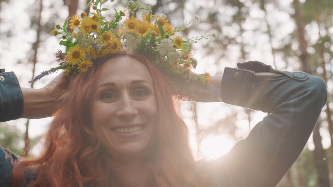 Portrait of joyful lady with red hair decorating her head with bright wildflower bouquet in forest, smiling warmly under sunlight, expressing happiness, creativity, and harmony with nature