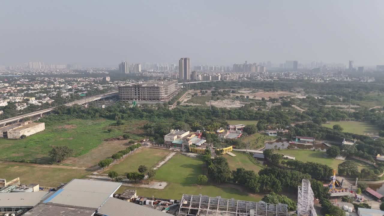 High-altitude shot of Noida highlighting planned residential blocks, green parks, and elevated roads set against a vast and expanding skyline