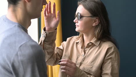 mujer ciega con gafas de sol tocando la cara de su novio cerca de una ventana en casa