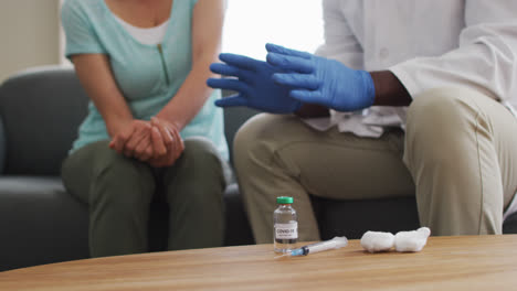 mid section of male african american doctor talking to female patient before injecting covid-19 vacc