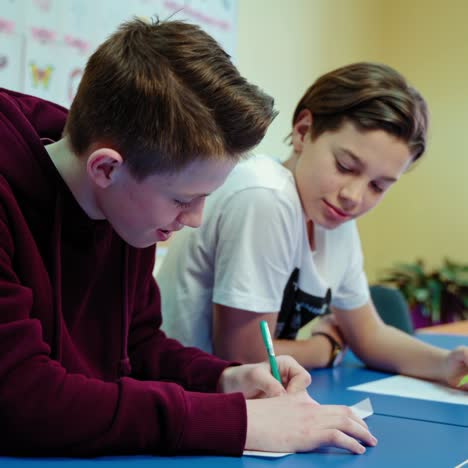 students studying at school. teenage boys sitting at the table and writing tasks in the modern classroom. educational process.