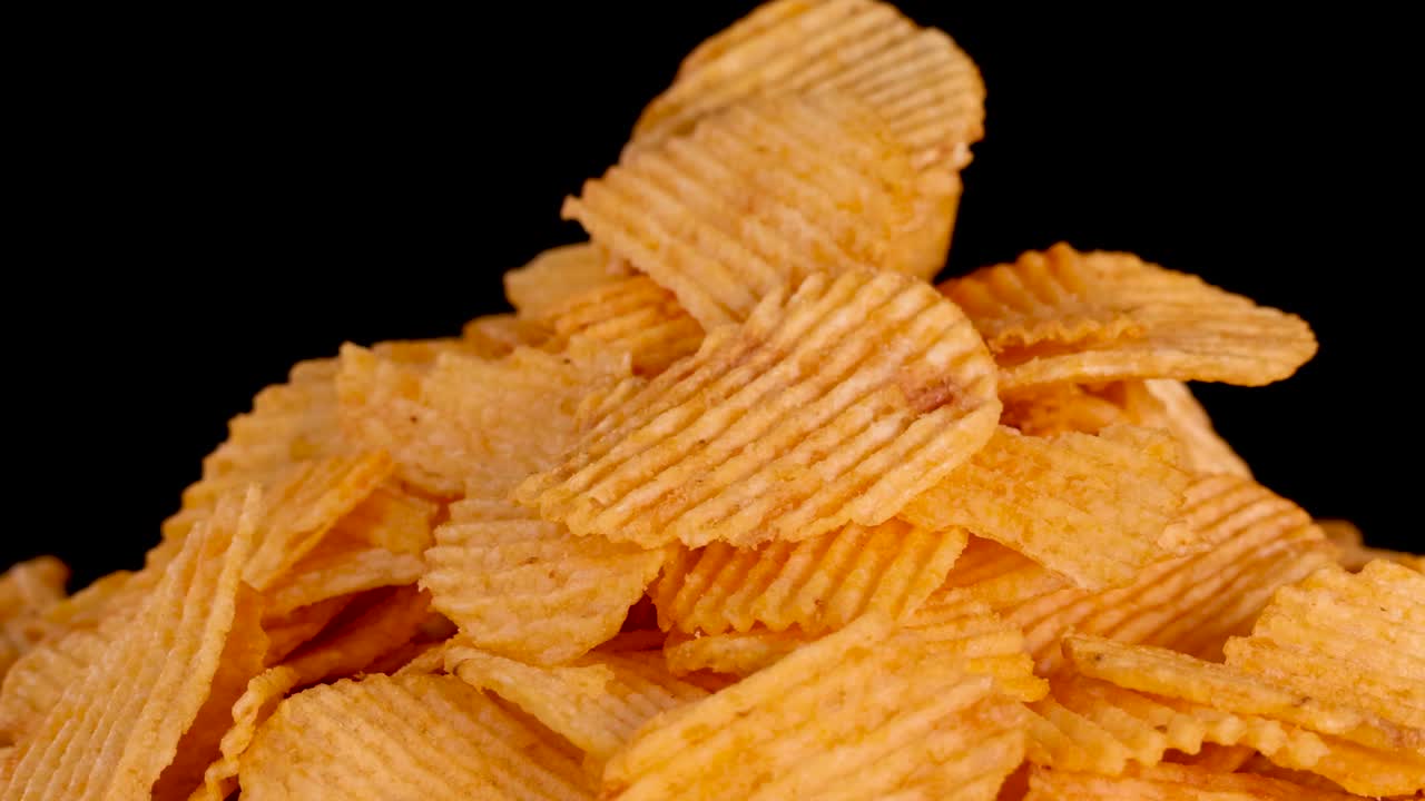 La telecamera zooma all'indietro da un primo piano di patatine fritte ondulate su sfondo nero, illuminazione uniforme
