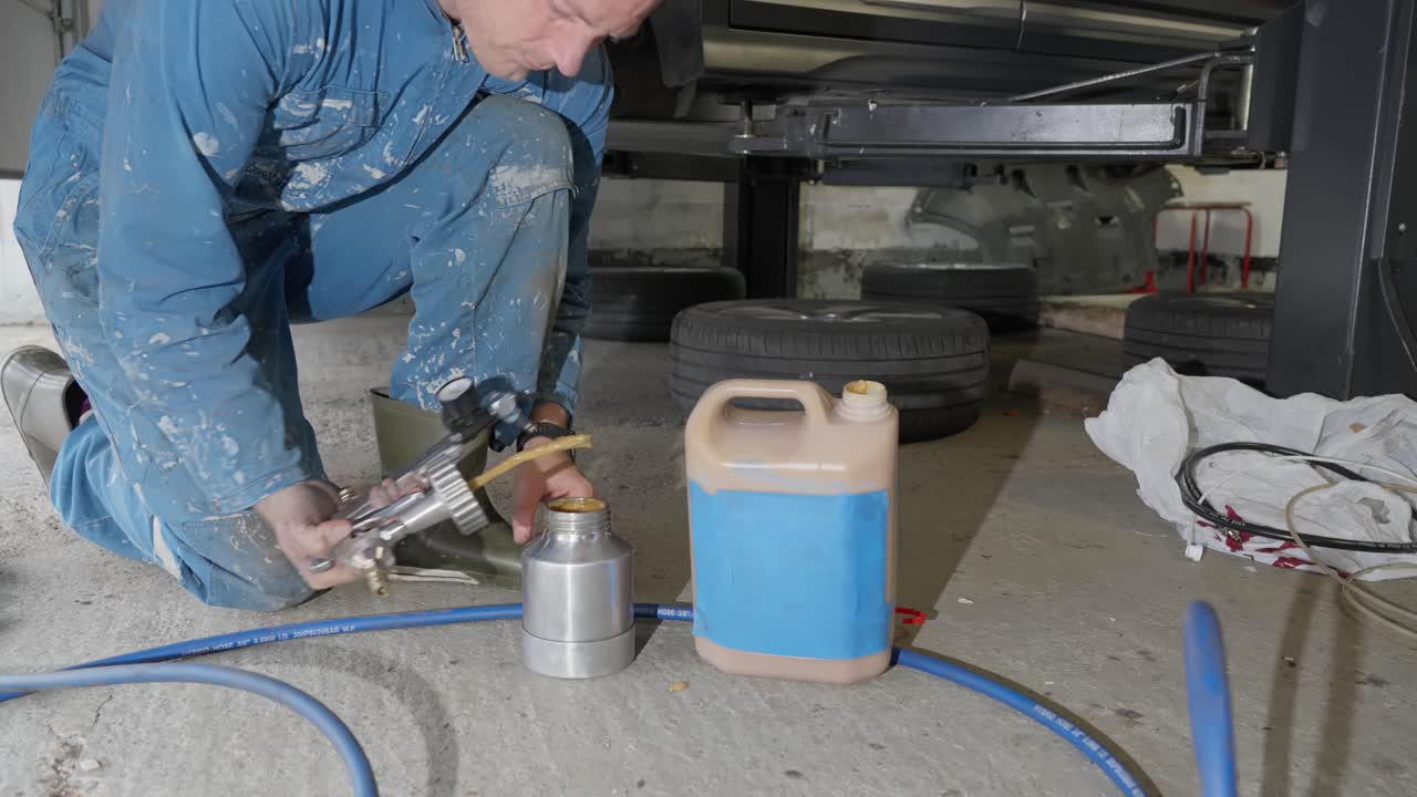 Man in garage adds natural and non toxic lanolin based rustproofing product to spray gun for car under body treatment