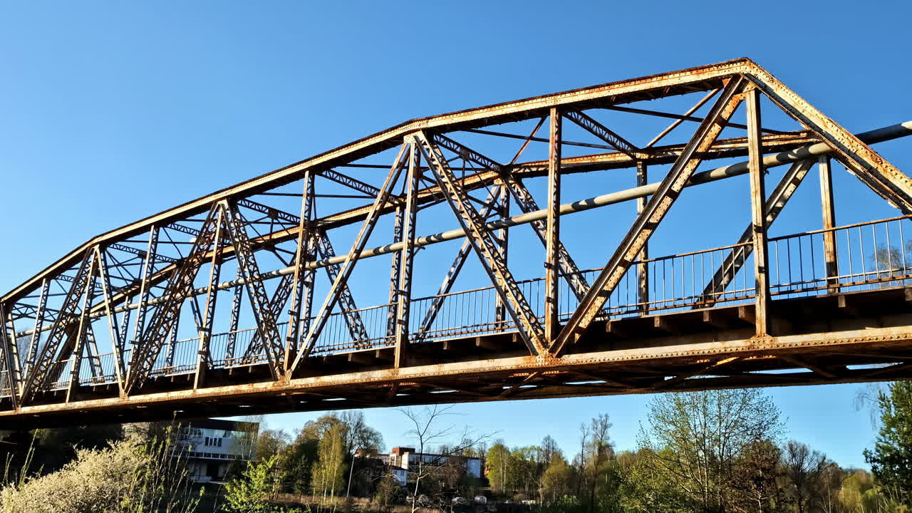 Rusted steel bridge spans tree-lined river on a sunny spring morning