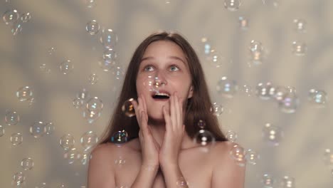appealing brunette girl playing with soap bubbles and looking at the camera slow motion close up shot of a young model with long hair opens her eyes and sees many soap bubbles flying around her girl looking happy and surprised playing with bubbles skincare concept slow motion