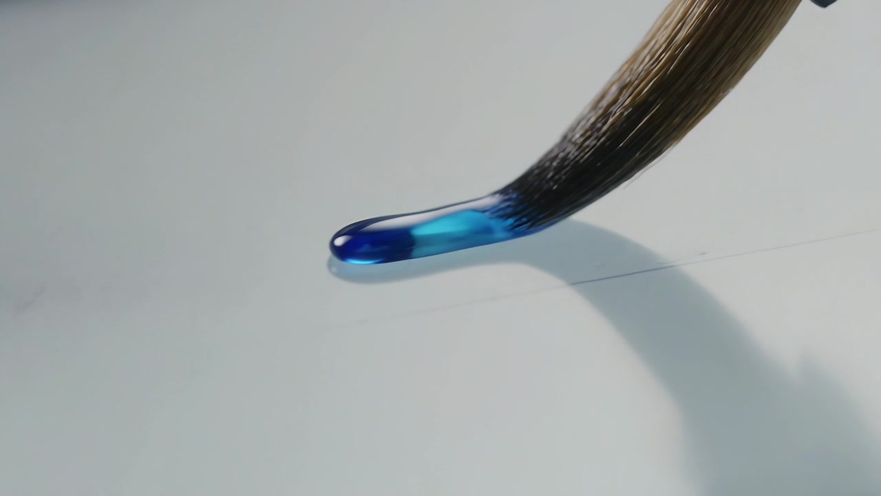 Spitze Pinselspitze mit blauer Perle zieht Flüssigkeit auf weißem Blatt entlang einer Bleistiftführung.