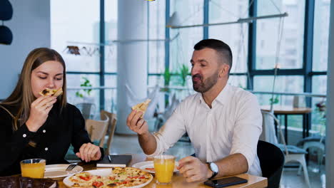 man and woman sit in café and have lunch. business people smell pizza, eat it and enjoy. colleagues have a talk during meals.