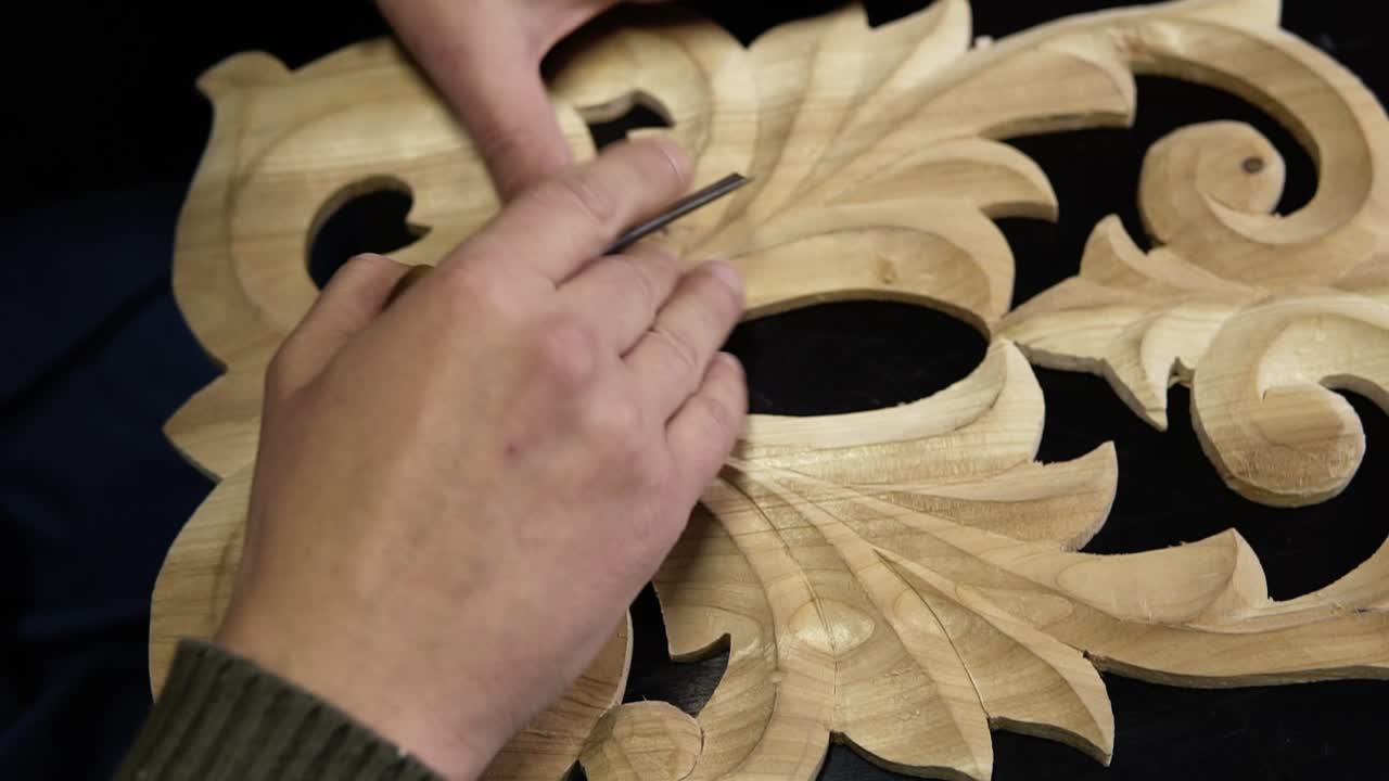 Close up footage of man's hands taking the right tool for curving a small details on the piece wodden pattern - floral ornament in work shop on the work table. Footage from the top