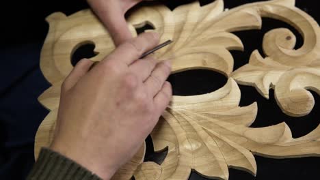 Close-up-footage-of-man's-hands-taking-the-right-tool-for-curving-a-small-details-on-the-piece-wodden-pattern---floral-ornament-in-work-shop-on-the-work-table.-Footage-from-the-top