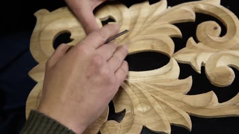 close up footage of man's hands taking the right tool for curving a small details on the piece wodden pattern - floral ornament in work shop on the work table. footage from the top