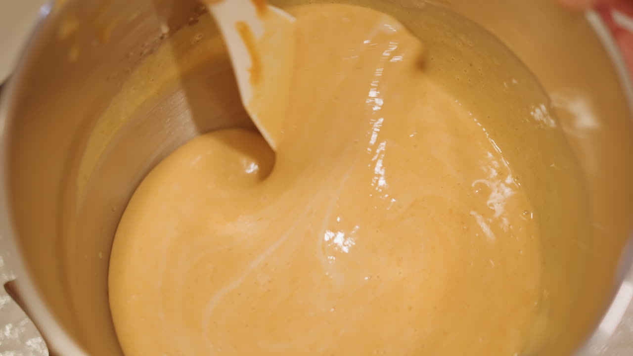 Satin pumpkin custard being stirred pastry chef briskly stirs silky pumpkin custard in metal bowl, glossy texture, steady motion, warm amber tones, countertop with parchment, professional technique