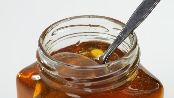 ein metalllöffel wird eingetaucht, um honig in ein glas auf weißem hintergrund zu nehmen. honig tropft aus einem metalllöffel, gesunde organische dicke honig nahaufnahme, süßes honig dessert 4k. slow motion