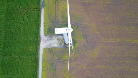 Top-down-aerial-view-rotating-above-wind-turbines-spinning-blades-on-rural-cultivated-farmland
