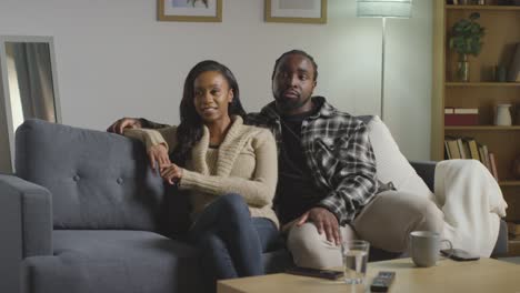 loving young couple relaxing at home sitting on sofa watching tv and talking together