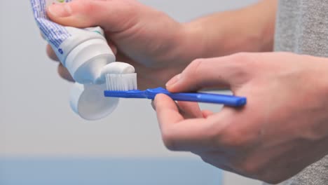 a woman in the bathroom squeezes white toothpaste from a tube onto a blue toothbrush on a white background, brushing her teeth, morning and evening procedures, hygiene