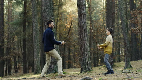 cheerful caucasian father and little son playing in the forest with sticks like they fighting with swords