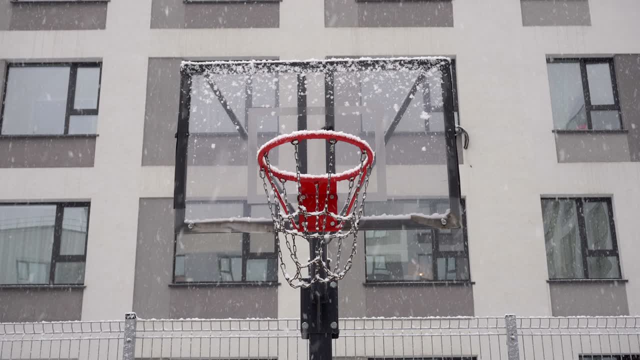 Basketball court in winter. Basketball backboard against the background of an apartment building during a snowfall