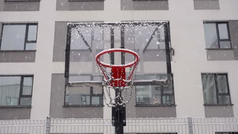 basketball court in winter. basketball backboard against the background of an apartment building during a snowfall