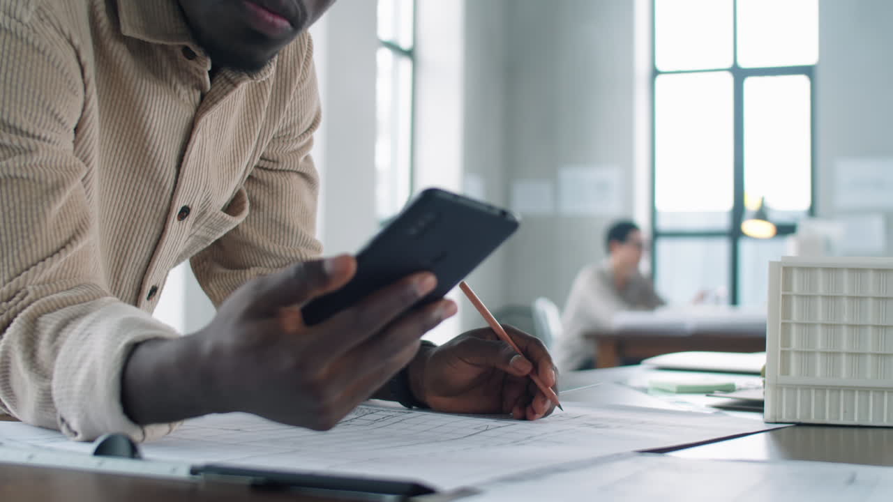 Architecte afro-américain dessinant un plan et utilisant son smartphone