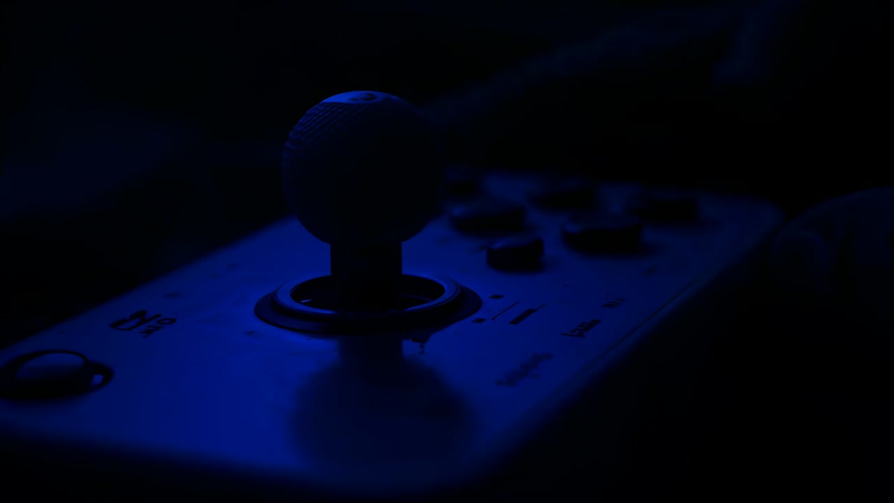 Pressing fingertip, hand in dark sleeve nudging joystick forward at blue arcade to control play