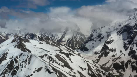 Air-flight-through-mountain-clouds-over-beautiful-snow-capped-peaks-of-mountains-and-glaciers.