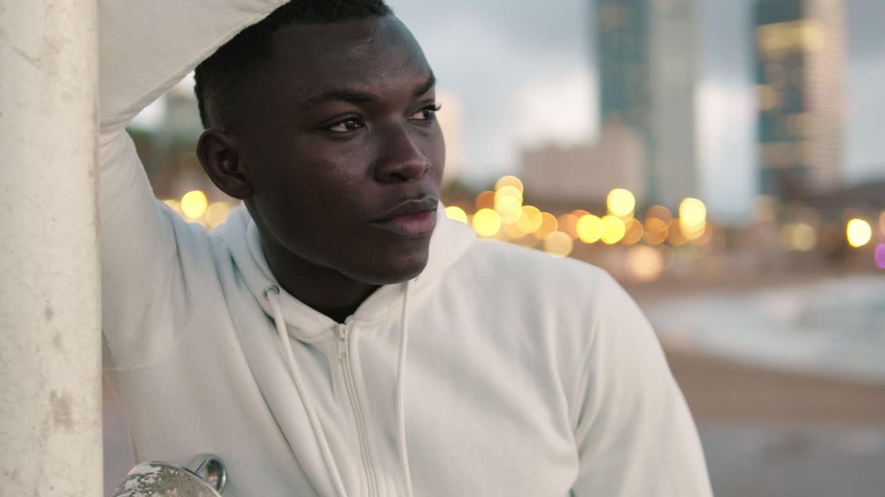 Pensive Young African American Man in White Hoodie at Night