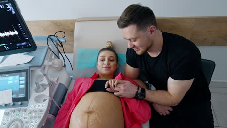 pretty caucasian woman expecting a baby lies on the doctor's couch. supportive husband talks to his wife. top view.