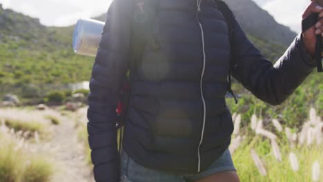 Mid-section-of-african-american-woman-trekking-poles-walking-while-trekking-in-the-mountains